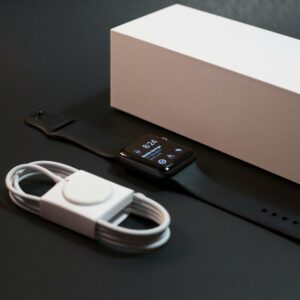 A modern smartwatch with charger displayed elegantly alongside its packaging on a dark surface.