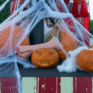 Spooky Halloween scene featuring carved pumpkins, faux cobwebs, and a decorative mannequin hand outdoors.
