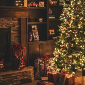 Warm holiday scene of a decorated Christmas tree with gifts by a cozy fireplace.