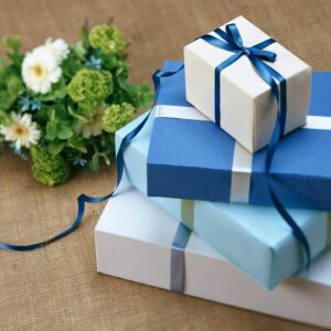 Three beautifully wrapped gift boxes with blue ribbons arranged beside a floral bouquet.
