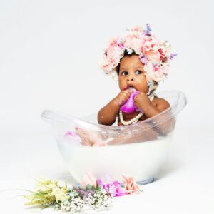 Charming baby in a milk bath adorned with a floral crown and pearls, surrounded by flowers.