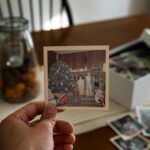 Hand holding an old Christmas photo against a backdrop of family pictures and seasonal decor.