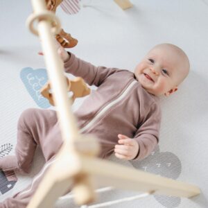 A joyful baby lying on a soft mat, playing with wooden toys, smiling brightly.