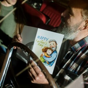 Father holding a Father's Day card inside a car, enjoying quality time with daughter.
