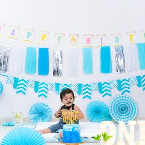 Happy ethnic child sitting near decorative balloons and festive cake while looking away