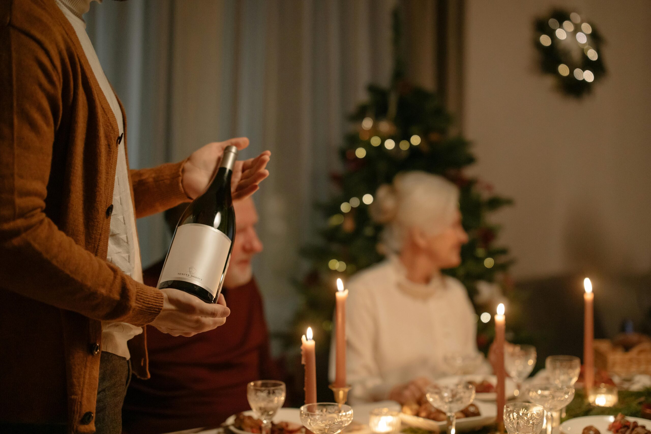 pexels photo 6185404 6185404 Cozy family gathering around a dinner table during the Christmas season with wine and festive decorations.