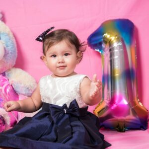 A cute baby in a birthday dress celebrates her first birthday with colorful decorations.