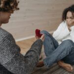 A man proposing to a woman indoors with a red ring box, capturing a moment of surprise and joy.