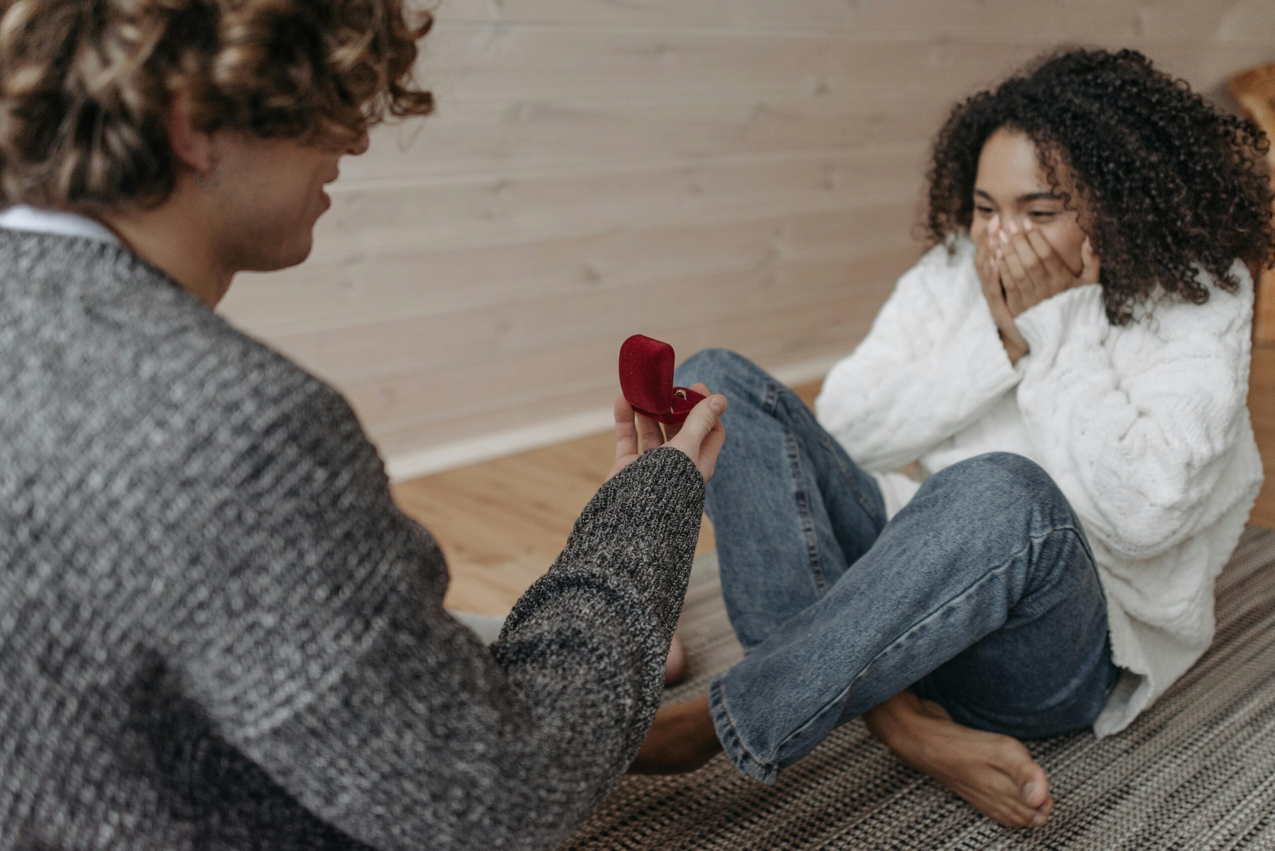 pexels photo 6549798 6549798 1 A man proposing to a woman indoors with a red ring box, capturing a moment of surprise and joy.