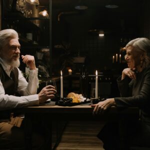 An elderly couple sharing a romantic dinner with candles and wine in a cozy room.