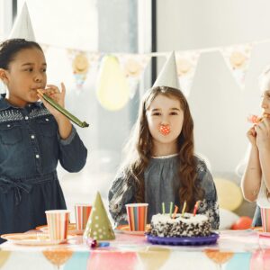 A lively birthday celebration with children in party hats enjoying cake and festivities indoors.