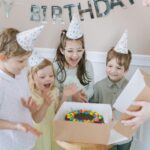 Joyful kids celebrating a birthday with a colorful cake and party hats indoors.