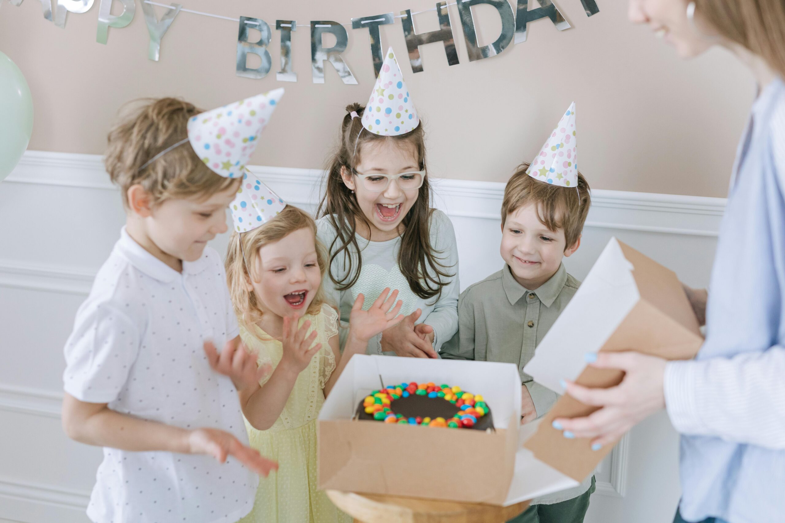 pexels photo 7600387 7600387 Joyful kids celebrating a birthday with a colorful cake and party hats indoors.