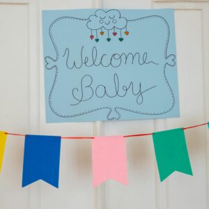 Cheerful baby shower decorations with colorful banner and welcome sign displayed indoors.