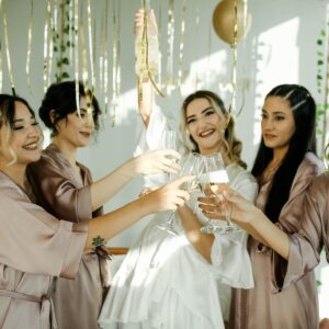 Group of women celebrating a bachelorette party with champagne in stylish robes.