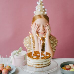 A young girl celebrates her birthday with cake and lollipops, wearing a party hat and gold dress.